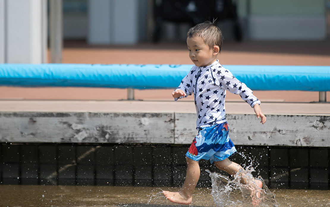 じゃぶじゃぶ池で水しぶきを上げて走るこども